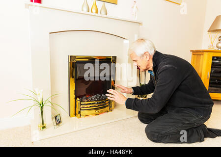 OAP cercando di mantenere caldo il riscaldamento le mani vicino al fuoco conservando le fatture verso il basso non può permettersi il riscaldamento bill elevata di gas le bollette di energia di calore termico titolare di pensione o di rendita in povertà Foto Stock