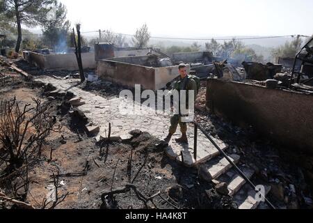 Halamish. 27 Nov, 2016. Un soldato israeliano sta di guardia accanto a una casa bruciata nel Halamish insediamento nella West Bank, su nov. 27, 2016. Decine di case sono state bruciate e quattro persone sono state ferite durante la notte come un incendio scoppiato nell'insediamento ebraico in Cisgiordania. Credito: Gil Cohen Magen/Xinhua/Alamy Live News Foto Stock