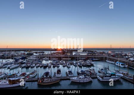Tramonto sul mare e il Porto di Ramsgate nel Kent, Inghilterra. Il marina Yachting in primo piano. Il sorgere del sole sopra il mare in sottile fascia arancione nel cielo azzurro. Foto Stock
