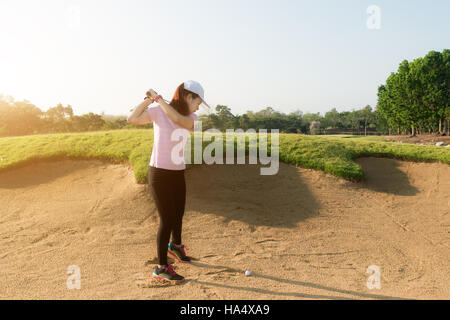 Donna asiatica giocatore di golf di colpire la pallina da golf al di fuori della trappola di sabbia. Golf sport concept. Foto Stock