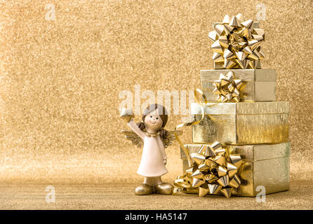 Vacanze di Natale decorazione. Confezioni regalo e il piccolo angelo luminoso su sfondo dorato Foto Stock