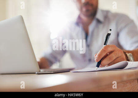 Immagine ravvicinata di giovani business man mano con la penna scrivere appunti su un foglio di carta. Executive maschio seduta a tavola presso l'ufficio domestico. Foto Stock