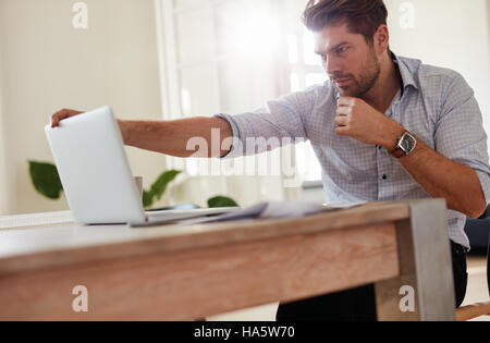 Colpo di giovane imprenditore seduta a tavola con il computer portatile. Uomo caucasico lavorando sul computer portatile. Foto Stock