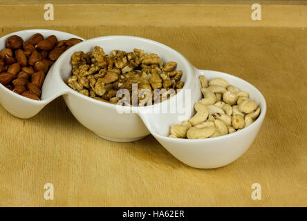 Tre tipi di dadi freschi ,Indian mandorle,(Macadamia) noci, nocciole in una ciotola bianco. Mangiare sano . Chiudere, vista orizzontale. Foto Stock