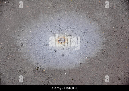 Una singola goccia di olio da un motore V8 si diffonde su asfalto bagnato per creare 'Rainbow' immagine Foto Stock
