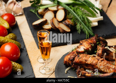 La carne fritta, patate, verdure, ortaggi su nero lastre di ardesia e due bicchierini di Cognac Foto Stock