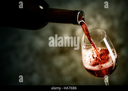 Il vino rosso viene versata nel bicchiere shot contro uno sfondo scuro Foto Stock
