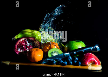 Tasto basso immagine di un piatto di frutti disposti attorno ad un bicchiere di acqua con un arancione schizzi nell'acqua. Foto Stock