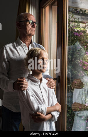 Nonno e nipote guardando fuori dalla finestra insieme. Foto Stock