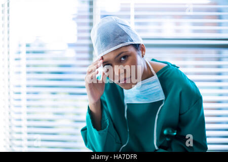 Ritratto di teso chirurgo femmina seduto in corridoio Foto Stock