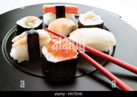 Vari sushi su una piastra nera con bacchette Foto Stock