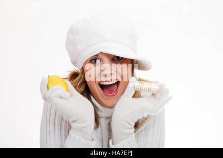 Giovane donna in un bianco turtleneck felpa con cappello di lana tenendo un limone e vitamina compresse Foto Stock