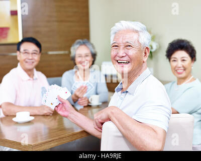 Senior uomo asiatico guardando fotocamera a sorridere mentre giocando a carte con gli amici. Foto Stock