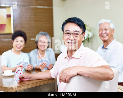 Senior uomo asiatico guardando fotocamera a sorridere mentre giocando a carte con gli amici. Foto Stock