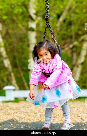 Adorabile bambina gioca nel parco giochi, ritorto sul distributore rotazione Foto Stock