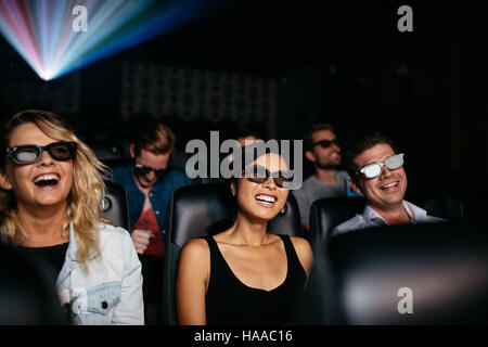 Un gruppo di giovani amici a guardare film in 3d in teatro e ridere. Giovani uomini e donne che indossano occhiali 3D in sala cinema. Foto Stock