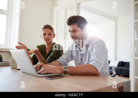 Colpo di coppia giovane seduti insieme a tavola e di lavoro sul computer portatile. Il giovane e la donna di casa utilizzando laptop. Foto Stock