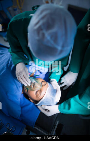 Chirurgo regolando le maschere di ossigeno sulla bocca del paziente nel teatro di funzionamento Foto Stock