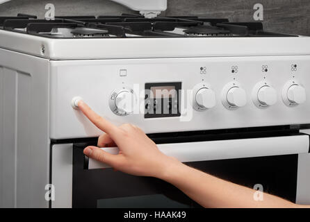 Femmina girando a mano sulla cucina bianca stufa a gas su sfondo grigio Foto Stock