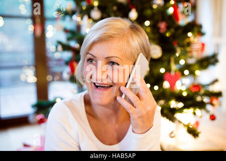Donna senior con lo smartphone nella parte anteriore dell'albero di Natale. Foto Stock