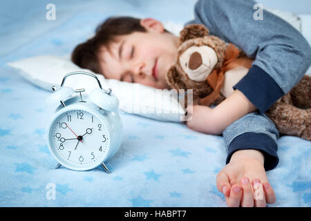 Sei anni bambino che dorme nel letto con la sveglia Foto Stock