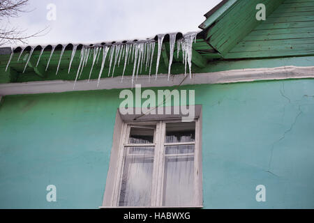 Ghiaccioli sul tetto verde della vecchia casa Foto Stock