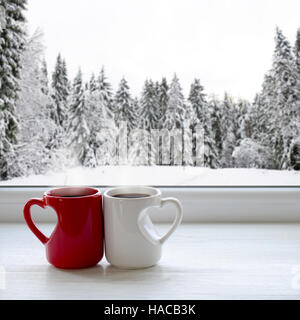 Due tazze di caffè su un davanzale. Sullo sfondo di una splendida foresta di inverno nella neve Foto Stock