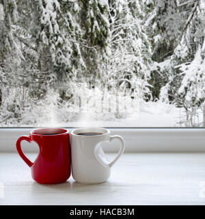 Due tazze di caffè su un davanzale. Sullo sfondo di una splendida foresta di inverno nella neve Foto Stock