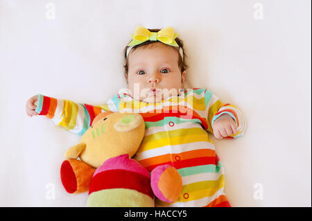 Faccia di carino sorpreso il bambino neonato ragazza in pigiama colorato con un arco sulla sua testa, rendere divertente l'espressione di bocca. Foto Stock