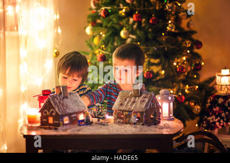 Due ragazzi dolce, fratelli, rendendo gingerbread cookies house, la decorazione a casa nella parte anteriore dell'albero di Natale, bambini che giocano e godendo di Natale c Foto Stock