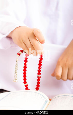 Ragazzo musulmano in Ramadan , Lettura Quraan , rendendo zikr utilizzando rosario Foto Stock