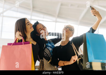 Attraente abbastanza donne tenendo selfie dopo lo shopping. Le ragazze sono molto felice e sorridente. Essi che posano per una foto. Hanno molte borse per lo shopping Foto Stock