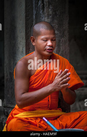 Un monaco buddista si siede con le mani giunte e gli occhi chiusi i canti preghiere nell'antico tempio di Angkor Wat, Siem Reap, Cambogia. Foto Stock