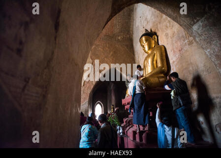 Persone che diano alle offerte di un Golden statua del Buddha presso il Tempio Sulamani a Bagan, Myanmar. Foto Stock