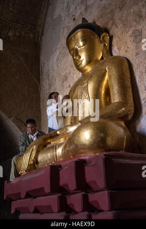 Persone che diano alle offerte di un Golden statua del Buddha presso il Tempio Sulamani a Bagan, Myanmar. Foto Stock