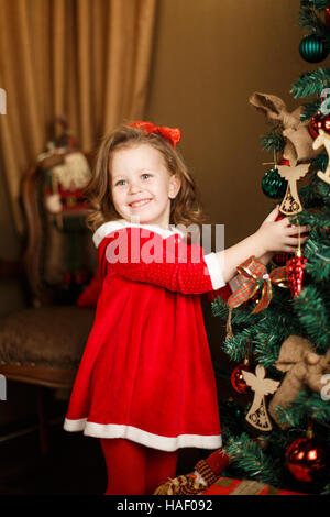 Ragazza permanente decorazioni mette a un albero di Natale. Ind verticale Foto Stock