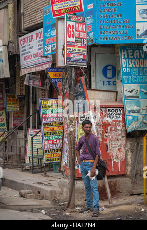 Un uomo in piedi su un angolo di strada nella Vecchia Delhi, India, shwoing una massa di advertisinf cartelloni per negozi e servizi. Foto Stock