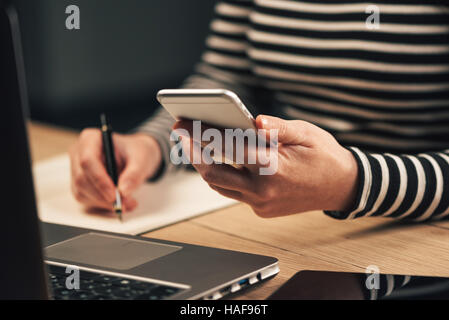 Donna iscritto elenco dei contatti dal telefono mobile nella sua agenda di business notebook per eseguire il backup Foto Stock