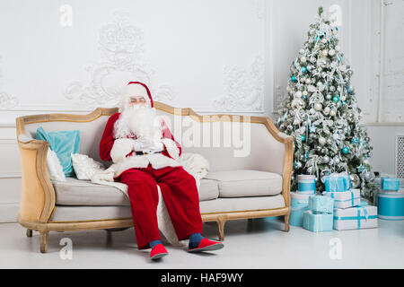 Tradizionale Santa Claus seduta sul divano e avente un resto. Natale. Sfondo rosso. Foto Stock