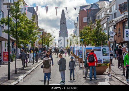 Le persone, i turisti a piedi nel quartiere dello shopping di Reykjavik, Islanda e la chiesa luterana Hallgrimskirkja è visto. Foto Stock