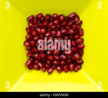 Il melograno rosso fresco semi in un contrasto di colore giallo brillante piatto. copia spazio su tutti i lati . Foto Stock