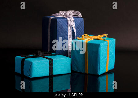 Tre presenta di diverse dimensioni avvolti in blu e turchese carta testurizzata legato con pizzi e nastri di velluto su nero Foto Stock