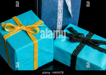 Tre presenta di diverse dimensioni avvolti in blu e turchese carta testurizzata legato con pizzi e nastri di velluto su nero Foto Stock