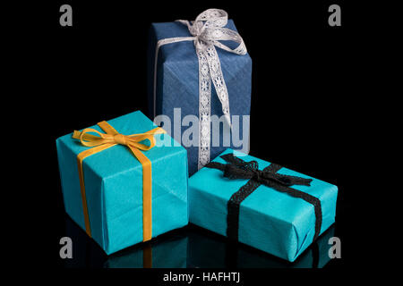 Tre presenta di diverse dimensioni avvolti in blu e turchese carta testurizzata legato con pizzi e nastri di velluto su nero Foto Stock
