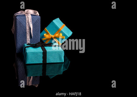 Tre presenta di diverse dimensioni avvolti in blu e turchese carta testurizzata legato con pizzi e nastri di velluto su nero Foto Stock