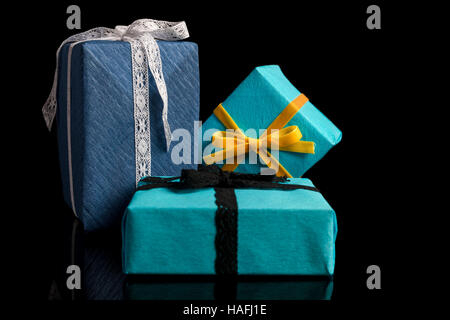 Tre presenta di diverse dimensioni avvolti in blu e turchese carta testurizzata legato con pizzi e nastri di velluto su nero Foto Stock