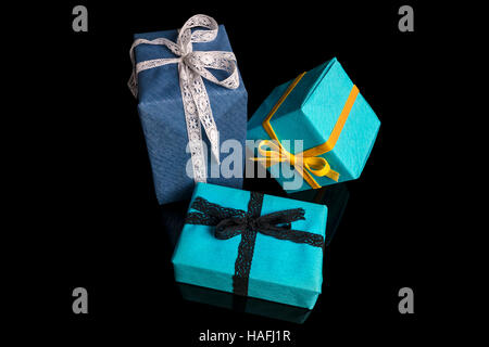 Tre presenta di diverse dimensioni avvolti in blu e turchese carta testurizzata legato con pizzi e nastri di velluto nero su closeu Foto Stock