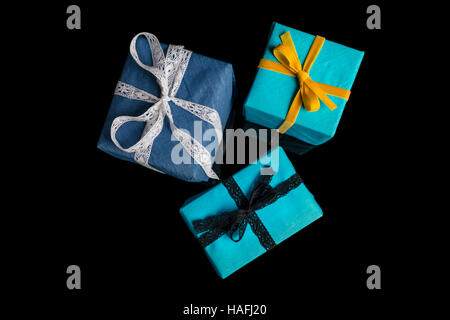 Tre presenta di diverse dimensioni avvolti in blu e turchese carta testurizzata legato con pizzi e nastri di velluto nero su direct Foto Stock