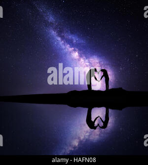 Via Lattea. Paesaggio notturno con cielo stellato e uomo e donna tenendo le mani a forma di cuore sulla montagna vicino al lago Foto Stock