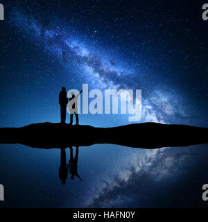 La Via Lattea con la silhouette di una famiglia. Padre e figlio che puntare il dito nella notte cielo stellato sulla montagna vicino al fiume Foto Stock